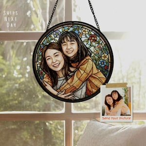 May include: A round, stained-glass style portrait of two smiling people, framed in black and hanging from a chain. The image is set against a window. A small photo with the text "Send Your Picture" is also visible.