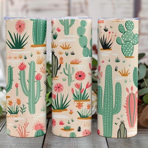 May include: Three cylindrical tumblers featuring a repeating pattern of various green cacti and pink desert flowers on a light beige background. Each tumbler has a flat lid and a smooth, straight-sided design with a consistent desert-themed print.