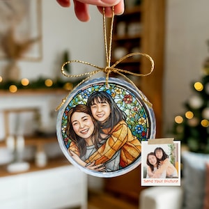 May include: A round, clear ornament with a gold string, featuring a stained-glass style illustration of two people hugging. The ornament has a floral border and a small photo with the text "Send Your Picture".