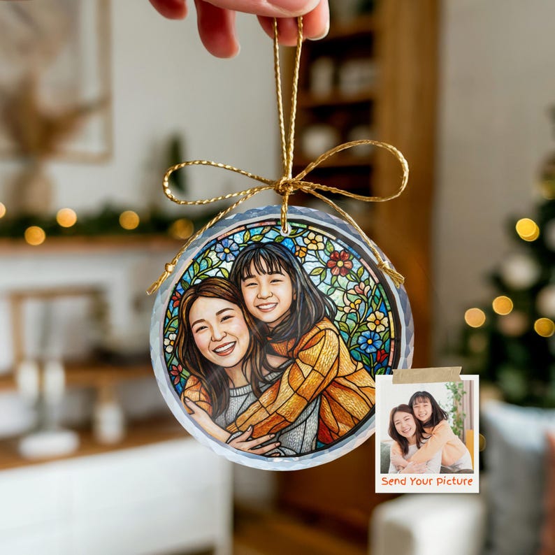 May include: A round, clear ornament with a gold string, featuring a stained-glass style illustration of two people hugging. The ornament has a floral border and a small photo with the text "Send Your Picture".