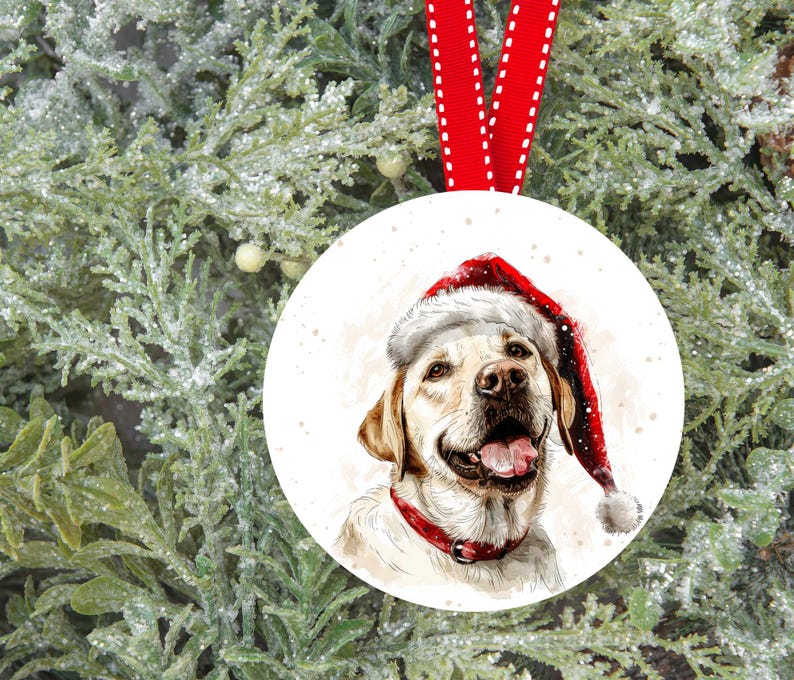 Pu&ograve; includere: Un ornamento natalizio in ceramica bianca con un'illustrazione ad acquerello di un labrador retriever giallo che indossa un cappello di Babbo Natale rosso. Il cane guarda lo spettatore con la lingua di fuori.