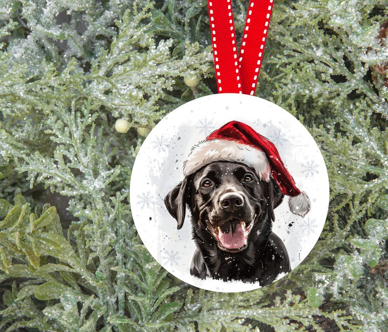 Pu&ograve; includere: Un Labrador Retriever nero che indossa un cappello rosso da Babbo Natale, su uno sfondo bianco innevato con fiocchi di neve. Il cane guarda direttamente lo spettatore con la bocca leggermente aperta, mostrando la lingua.