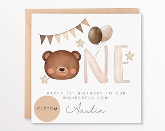 May include: A square birthday card with a brown teddy bear illustration, the word "ONE", balloons, stars, and a banner. The text reads "HAPPY 1ST BIRTHDAY TO OUR WONDERFUL SON!" and a custom name. The card is on a brown envelope.