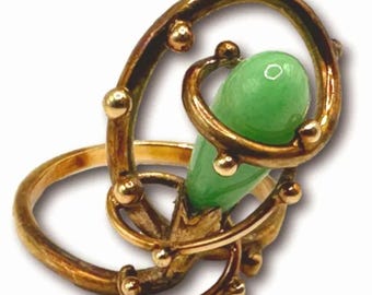 Könnte beinhalten: Ein goldener Ring mit einem grünen Jade-Stein, der in einem wirbelnden, komplizierten Design gefasst ist. Der Ring ist mit kleinen goldenen Perlen verziert.