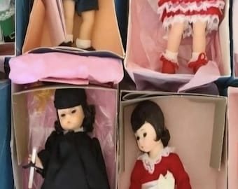 Könnte beinhalten: Vier Sammlerpuppen in einzelnen Kartons. Eine trägt einen blauen Hut und dunkle Shorts, eine ein rotes Kleid mit weißer Spitze, eine einen schwarzen Talar mit einer Urkunde und eine ein rotes Outfit mit weißer Schärpe. Das Wort SOLD ist zu sehen.