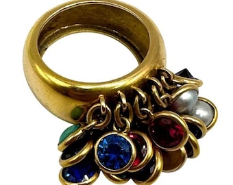 Könnte beinhalten: Ein goldfarbener Ring mit einem dicken Band und baumelnden Anhängern. Die Anhänger umfassen verschiedene farbige Edelsteine, darunter Blau, Rot und Grün, sowie einige Perlen. Der Ring hat eine Vintage-Ästhetik.