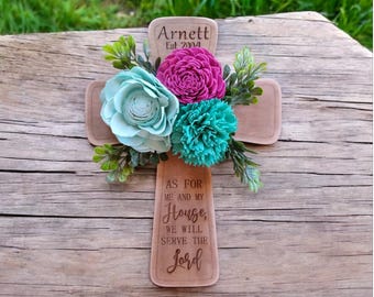 May include: Wooden cross with a floral arrangement of light blue, pink, and turquoise flowers. The cross is engraved with the text "Arnett Est 2004" and the quote "As for me and my house, we will serve the Lord."