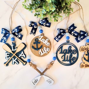 May include: A set of six nautical-themed ornaments featuring blue and white ribbon bows, wooden paddles, anchors, and the text "Lake Life".