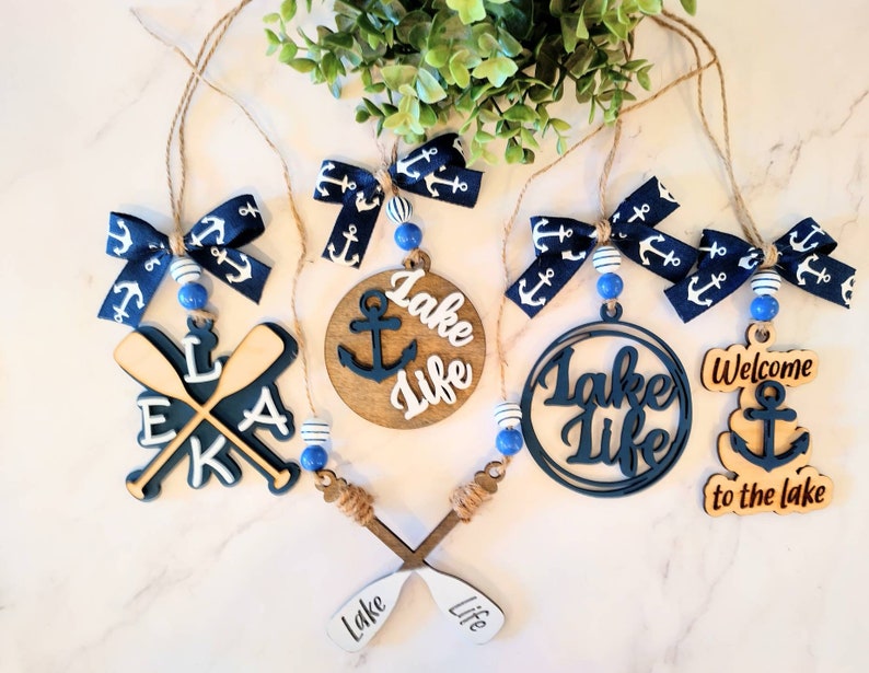 May include: A set of six nautical-themed ornaments featuring blue and white ribbon bows, wooden paddles, anchors, and the text "Lake Life".