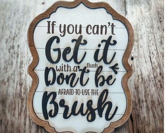 May include: Wooden sign with a decorative border and the text "If you can't Get it with a flush Don't be Afraid to use the Brush" in black lettering. The sign has a white background with horizontal wood grain lines.