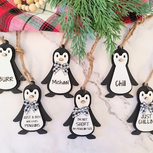 May include: Six black and white penguin ornaments with different sayings. The sayings include "Burr", "Just a boy who loves penguins", "Michael", "Chill", "I'm not short, I'm penguin size", and "Just chillin!"
