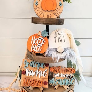 Op de afbeelding: Een etagère versierd met houten borden met een herfstthema en een kabouter. De borden bevatten zinnen als "Pumpkin Spice Keeps Me Nice", "Hello Autumn", "Grateful Thankful Blessed" en "Herfst is het bewijs dat verandering mooi is".