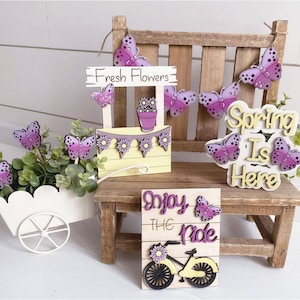 May include: Wooden spring-themed decorations with purple butterflies, flowers, and the text "Spring is Here" and "Enjoy the Ride".