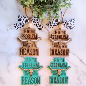 May include: Four wooden ornaments with the text "If I'm the problem, then you might be the reason." Two are natural wood, two are turquoise. Each has a bull skull design and a cow print bow.
