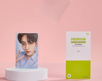 May include: A clear plastic sleeve for photo cards, with a green and white label that reads "PREMIUM PHOTO CARD SLEEVES 61 x 91mm No PVC & Acid Free". The label also has a number "50" on it.