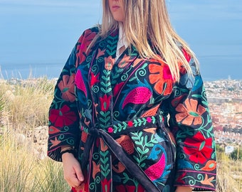 May include: A black embroidered jacket with a floral pattern in shades of red, pink, green, and blue. The jacket has a tie belt and long sleeves.
