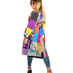 K&ouml;nnte beinhalten: Ein langer, bunter Patchwork-Mantel mit G&uuml;rtel. Der Mantel besteht aus verschiedenen Stoffen und Mustern, darunter Blumen, geometrische Muster und Paisley. Das Model tr&auml;gt den Mantel mit Jeans und schwarzen Schuhen.