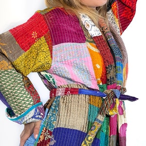 K&ouml;nnte beinhalten: Eine bunte Patchworkjacke mit einem Bindeg&uuml;rtel. Die Jacke besteht aus verschiedenen Stoffen und Farben, darunter Rot, Rosa, Blau, Gr&uuml;n, Gelb und Braun.