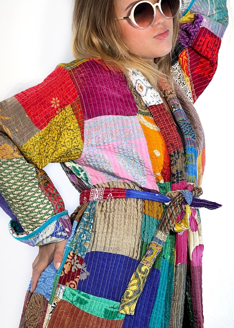 K&ouml;nnte beinhalten: Eine bunte Patchworkjacke mit einem Bindeg&uuml;rtel. Die Jacke besteht aus verschiedenen Stoffen und Farben, darunter Rot, Rosa, Blau, Gr&uuml;n, Gelb und Braun.