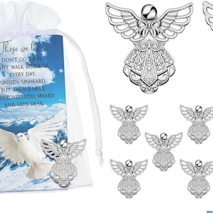 May include: A set of silver-toned angel pins with intricate wing and dress detailing. Each pin features a secure back clasp. Included is a white organza drawstring bag and a memorial card with a white dove and the text: Those we love, don't go away, they walk beside us every day, unseen, unheard, but always near, still loved, still missed, and very dear.