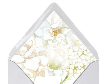 Pode incluir: Envelope branco com um design floral com flores brancas e folhas verdes. As flores são pintadas em estilo aquarela.