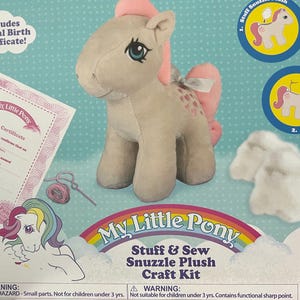 May include: A My Little Pony "Snuzzle" plush craft kit. The kit includes a plush pony, stuffing, a birth certificate, and instructions. The pony is light gray with a pink mane, tail, and heart-shaped markings.