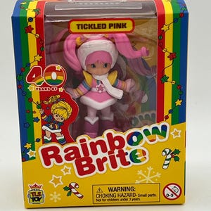 May include: A Tickled Pink Rainbow Brite doll in a pink and white winter outfit with a pink hat and pigtails. The doll is packaged in a yellow box with a rainbow design and the text "40 Years of Rainbow Brite".