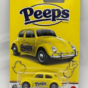 May include: A yellow Matchbox car featuring a Volkswagen Beetle design, branded with "Peeps" and a bunny graphic. The packaging is yellow with the Matchbox logo and "Peeps" branding. The car is a die-cast model.