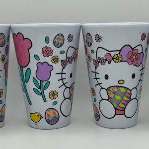 May include: Set of four white plastic cups with a Hello Kitty Easter design. The cups feature Hello Kitty holding a colorful Easter egg, surrounded by flowers, tulips, and a chick.