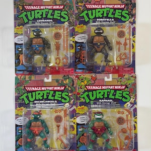 May include: Four Teenage Mutant Ninja Turtles action figures, each packaged on a colorful card. The figures are Leonardo, Donatello, Michelangelo, and Raphael, each with their signature weapons and accessories. The packaging includes the text "Teenage Mutant Ninja Turtles" and "With Storage Shell."