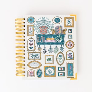 May include: A spiral-bound reading planner with a white cover featuring a teal shelf illustration. The shelf holds books labeled 'the READING PLANNER' and a potted plant. Surrounding the shelf are various framed botanical and animal art prints.
