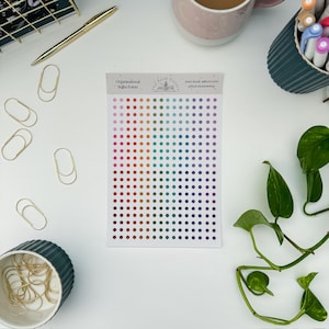 May include: A sheet of colorful dot stickers for organizational use. The dots transition from red to purple, with text that reads "Organizational Bullet Points" and "the book sisters". Gold paper clips and a pen are also visible.
