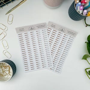 Peut inclure: Deux feuilles d'autocollants étoiles de notation avec le texte "100 Small Rating Stars" et "100 Large Rating Stars". Chaque feuille comporte des rangées de petites étoiles brunes. Les autocollants sont sur une surface blanche avec des fournitures de bureau.