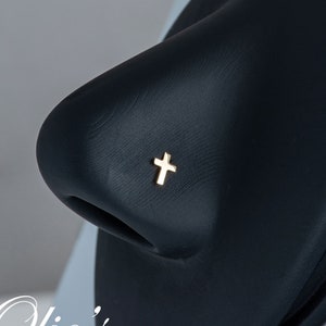 May include: A gold cross nose ring on a black nose piercing model.