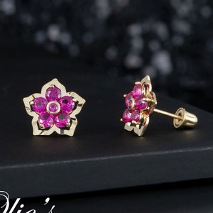 May include: A pair of gold flower-shaped earrings with pink gemstones. The earrings have a post back.