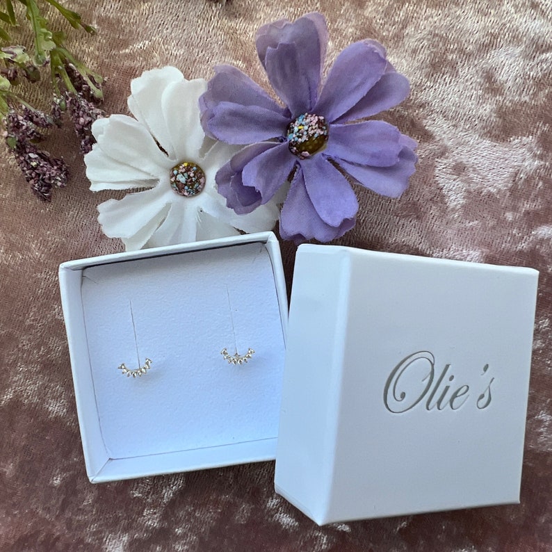 May include: A pair of silver hoop earrings with a delicate, curved design, displayed in a white box with the text "Ollie's" on the lid.