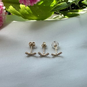 May include: Three pairs of gold earrings with a curved design and small clear stones. The earrings have a post back.