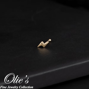 May include: Gold lightning bolt nose ring piercing jewelry.