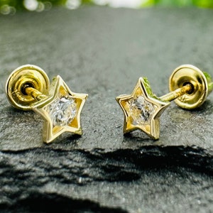 May include: A pair of gold star-shaped earrings with a clear stone in the center. The earrings have a screw-back closure.