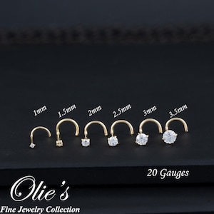May include: A collection of gold nose rings with varying sizes of clear gemstones. The sizes range from 1mm to 3.5mm. The text "20 Gauges" is also visible. The jewelry is from Olie's Fine Jewelry Collection.