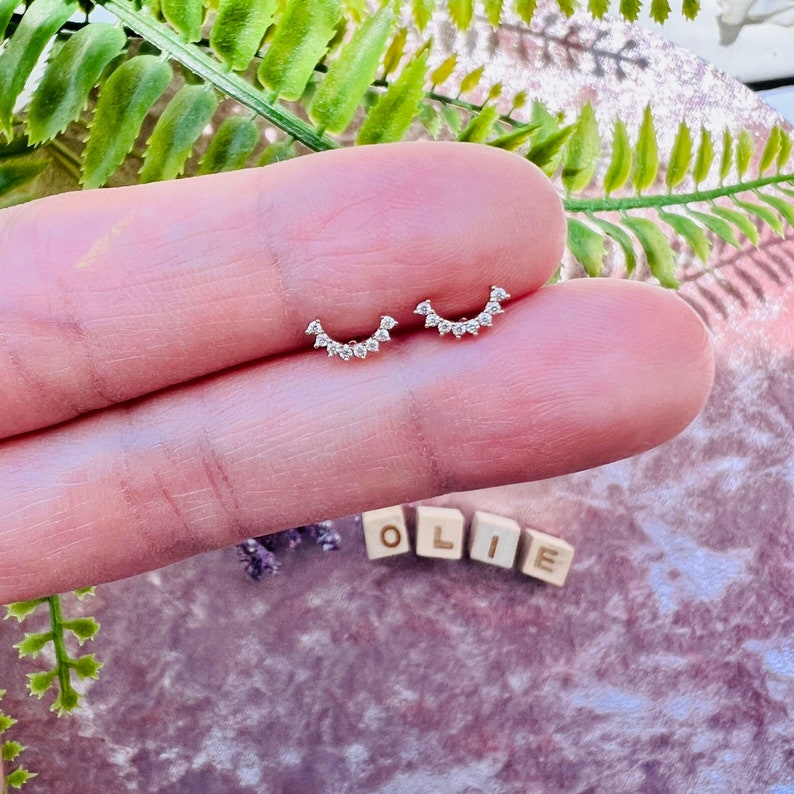 May include: A pair of silver earrings with a crescent moon shape and small clear stones.