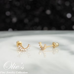 May include: A pair of gold earrings with a crescent moon design set with small clear stones. The earrings have a post and butterfly back.