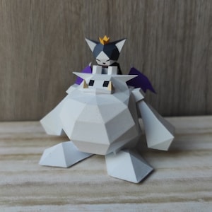 Puede incluir: Un monstruo de papel blanco con alas moradas y un gato blanco y negro con una corona dorada montado en su espalda.