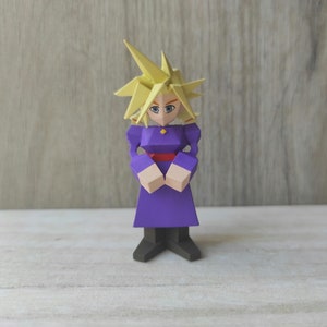 Puede incluir: Una figurita de papel de color morado y amarillo que representa a un personaje con el pelo rubio de punta, un vestido morado y un cinturón rojo.