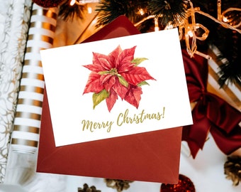 May include: A white card with a red poinsettia flower and the text "Merry Christmas!" printed in gold. The card is sitting on a red envelope.