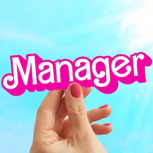 May include: A hand holds up a pink sign with the word "Manager" written in white letters.