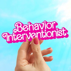 May include: A pink paper sign with the text "Behavior Interventionist" held up against a blue sky.