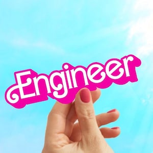 May include: A hand holds up a pink paper sign with the word "Engineer" written in white letters against a bright blue sky.