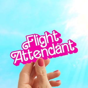 May include: A hand holds up a pink sign with the words "Flight Attendant" in white letters against a blue sky.