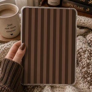 May include: A rectangular tablet case featuring a vertical striped pattern in alternating shades of dark brown and light brown. The case is encased in a clear, transparent protective shell with rounded corners, providing a sleek and simple aesthetic.